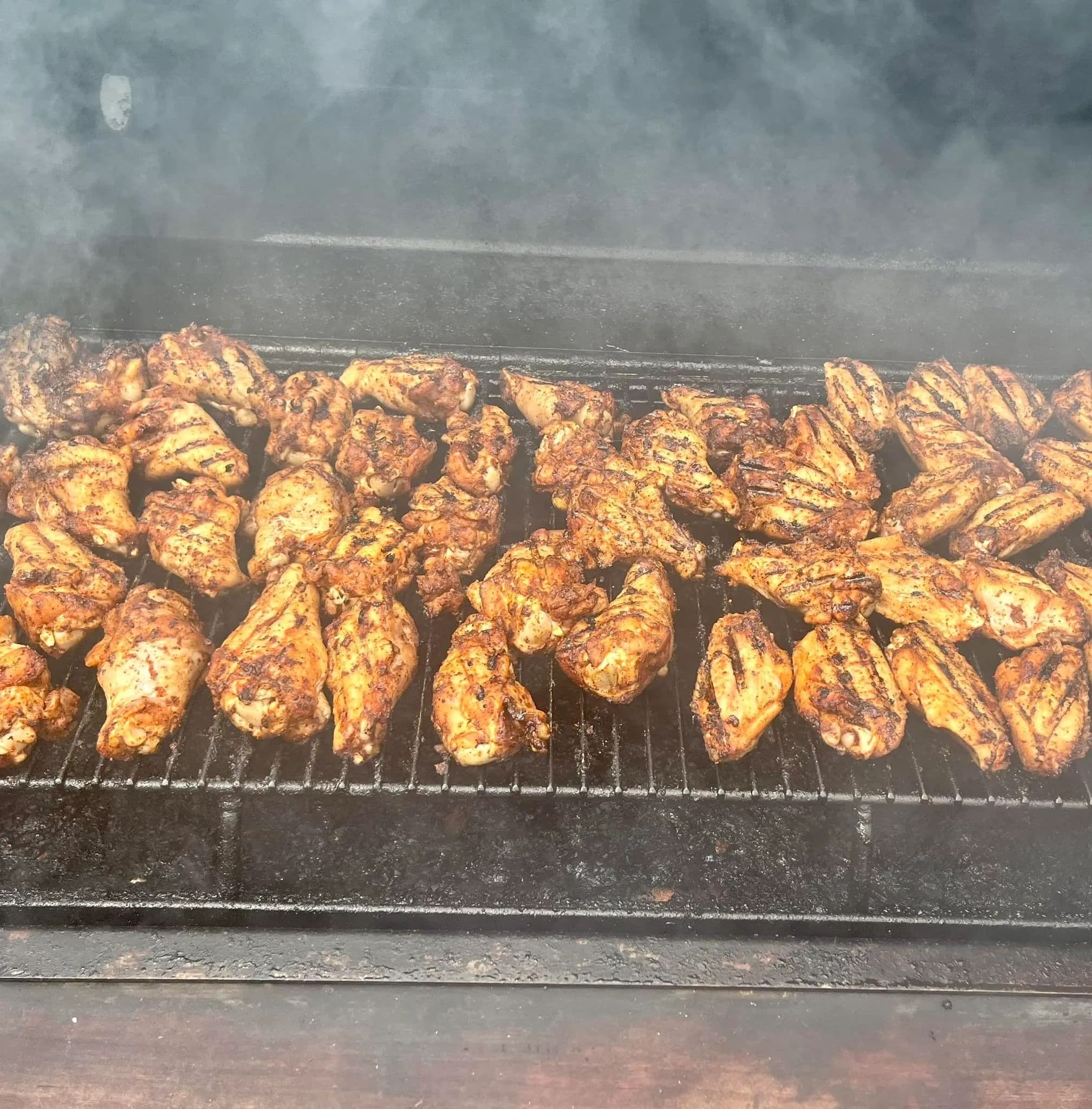 Chicken wings laid across the smoker rack at Lil' Piece BBQ, smoke rolling over them